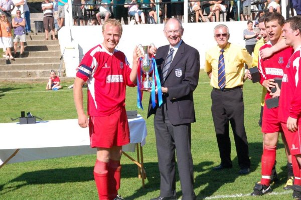 Taverners captain Tom Burridge accepts the cup from FA Joint Chairman Roger Burden